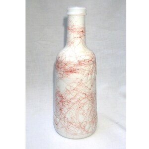 May include: White glass bottle with a red, string-like design. The bottle is clear and has a textured surface.