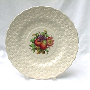 May include: A white ceramic saucer with a raised embossed pattern of small flowers. The center of the saucer features a colorful floral design with pears, grapes, and a flower.