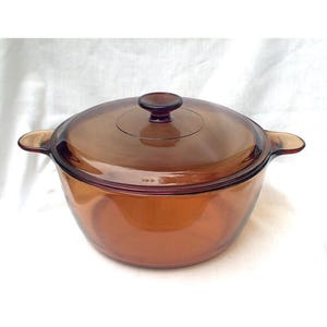 Puede incluir: Una cacerola de vidrio marrón con tapa y dos asas. La cacerola está hecha de vidrio templado y es apta para horno.