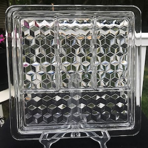 Puede incluir: Una bandeja de servir de vidrio transparente con un patrón geométrico en relieve. La bandeja tiene tres compartimentos.