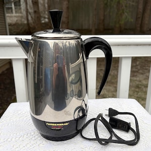 May include: A Farberware Superfast electric coffee percolator. The stainless steel coffee pot has a black handle, lid knob, and base. The power cord is black. The percolator is sitting on a white surface.