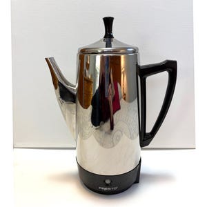 以下が含まれることがあります： 黒いベースとハンドルが付いた、ステンレス製のPrestoコーヒーパーコレーター。コーヒーポットには注ぎ口と黒いノブが付いた蓋が付いています。「PRESTO」の文字がベースに印刷されています。