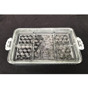 Puede incluir: Una bandeja de servir de vidrio transparente con cinco compartimentos. La bandeja tiene un borde elevado y dos asas a los lados. El fondo de la bandeja tiene un patrón de diamante.