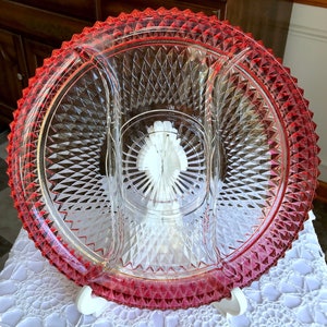 Può includere: Un piatto da portata in vetro trasparente con tre sezioni. Il piatto ha un motivo a forma di diamante in rilievo e un bordo rosso.