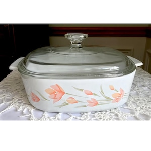 Puede incluir: Plato para hornear blanco con tapa de vidrio y un diseño floral con flores rosas y hojas verdes.