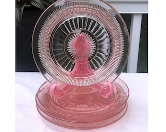 Puede incluir: Juego de cuatro platos de postre de vidrio rosa con un delicado patrón de estrella en relieve. Los platos están apilados en un soporte rosa.