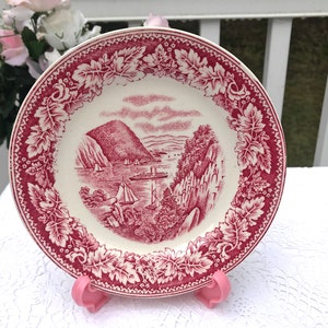 Puede incluir: Un plato de cerámica vintage rojo y blanco con un diseño escénico de una cordillera, una masa de agua y veleros. El plato tiene un borde decorativo de hojas rojas.