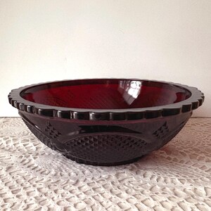 May include: A deep red glass bowl with a decorative rim and a textured diamond pattern. The bowl is a rich colour and appears to be made of thick glass. The bowl is likely vintage or antique.