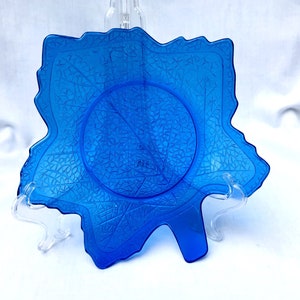 Op de afbeelding: Een kobaltblauwe glazen schotel in de vorm van een blad met een getextureerd oppervlak. De schotel staat op een witte achtergrond.