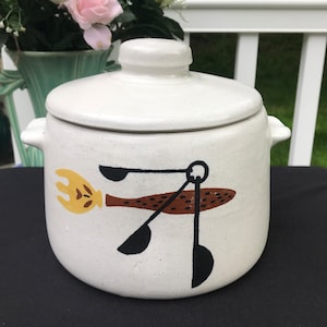 May include: White ceramic crock with a lid, featuring a brown and black design of a spoon, fork, and spatula. The design is stylised and abstract.
