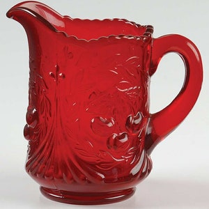 Könnte beinhalten: Eine rote Glaskanne mit einem Kirschendesign. Die Kanne hat einen gewellten Rand und einen Henkel.