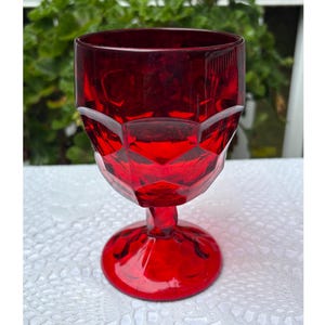 Puede incluir: Un cáliz vintage de color rojo rubí con un diseño facetado. El vaso tiene una base redonda, un tallo y un cuenco con un patrón geométrico. El cáliz está hecho de un material transparente y probablemente se utiliza para beber bebidas.