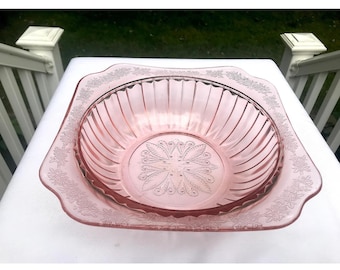 May include: A pink glass bowl with a square shape and a fluted design. The bowl has a floral pattern around the rim.