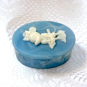 May include: An oval-shaped blue and white marbled trinket box featuring a raised, cream-colored relief of a cartoon mouse character on the lid. The box has a smooth, polished finish with swirling color patterns across the top and sides.