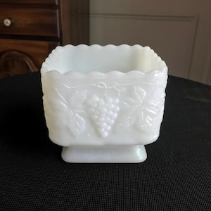 Könnte beinhalten: Weiße Milchglas Schüssel mit einem Traubenranken-Design. Die Schüssel hat eine quadratische Form mit einem gewellten Rand und einem erhöhten Boden.