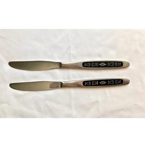 May include: Two silver butter knives with black handles featuring a decorative floral design.