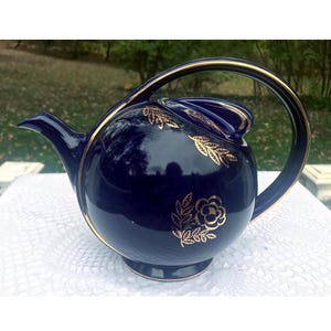 May include: Cobalt blue teapot with a gold trim and floral design. The teapot has a rounded body and a curved handle.