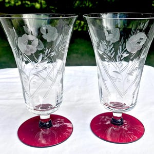 Puede incluir: Dos copas de vidrio transparente con un diseño floral grabado y una base de color rojo rubí.