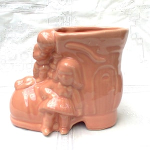 May include: A pink ceramic planter shaped like a shoe with two children figures on the side.