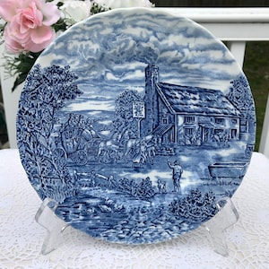 May include: Blue and white ceramic plate with a vintage scene of a horse-drawn carriage, a pub called "The Red Lion", and a country landscape.