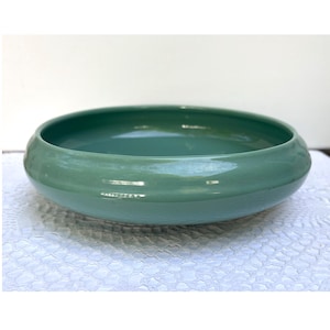 May include: A round, shallow, celadon-colored ceramic bowl. The bowl has a smooth, glossy finish and a wide, slightly curved rim. The bowl is likely used for decorative purposes or serving food.