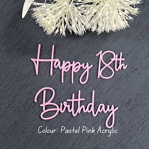 May include: A pastel pink acrylic cake topper with the words "Happy 18th Birthday" in a cursive font. The text "Colour: Pastel Pink Acrylic" is below the words. White floral accents are in the background.