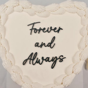 May include: A white heart-shaped cake with white frosting and a black inscription that reads "Forever and Always".