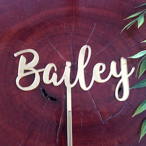Può includere: Topper per torta in acrilico a specchio dorato con il nome "Bailey" in un carattere corsivo.