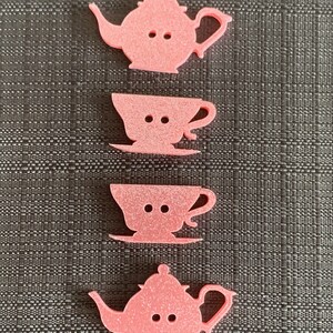 May include: Four pink felt teacup and teapot buttons. The buttons are shaped like teacups and teapots and have two small holes for sewing.