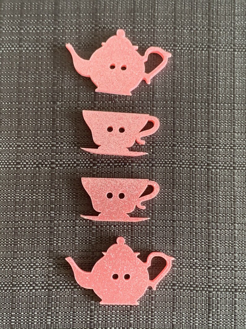 May include: Four pink felt teacup and teapot buttons. The buttons are shaped like teacups and teapots and have two small holes for sewing.