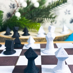 May include: A black and white chessboard with black and white dice pieces. The dice are shaped like a pyramid with a number on each side. The board is set up for a game of chess.