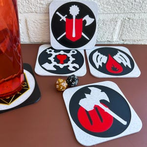 May include: Four white coasters with black and red designs. Each coaster features a different symbol, including a shield with crossed swords, a gear with a goblet, a pair of wings with a blood drop, and an axe with a red circle. Two dice are also visible on the table.