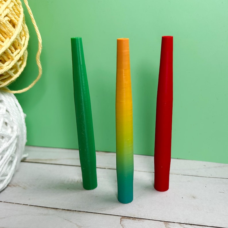 May include: Three slender, cylindrical tools stand upright. One is solid green, one is solid red, and the center tool features a vertical gradient transitioning from yellow at the top to green at the bottom. Each tool has a smooth, tapered design.
