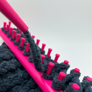 Close up of pink yarn guide feeding dark gray chunky yarn on pink knitting loom