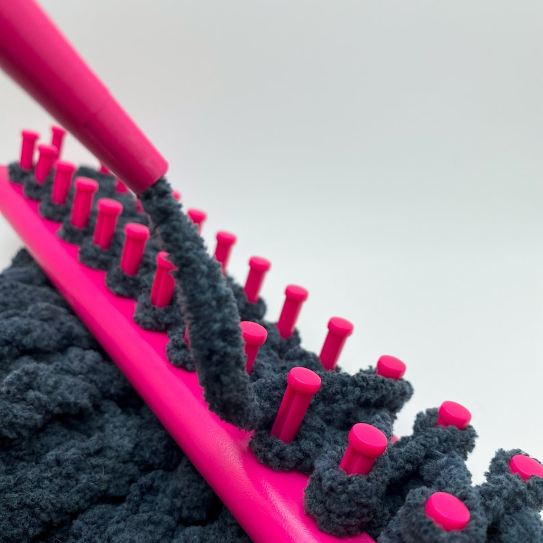 Close up of pink yarn guide feeding dark gray chunky yarn on pink knitting loom