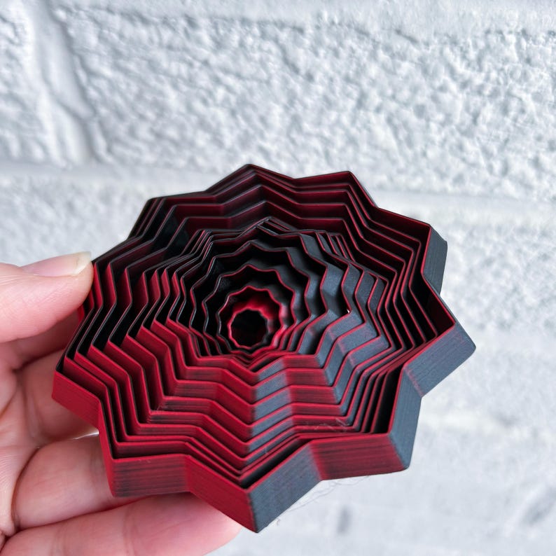 A pale hand holding a 3D printed fidget star in red and black.