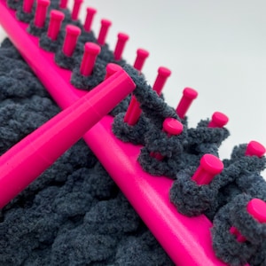 Close up of pink yarn guide feeding dark gray chunky yarn on pink knitting loom