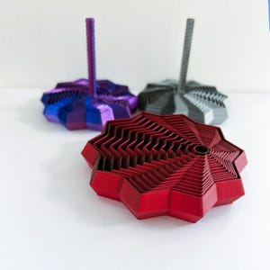 Three 3D printed fidget stars, one in red and black without a handle that is bigger, and two smaller multicolored stars with handles.