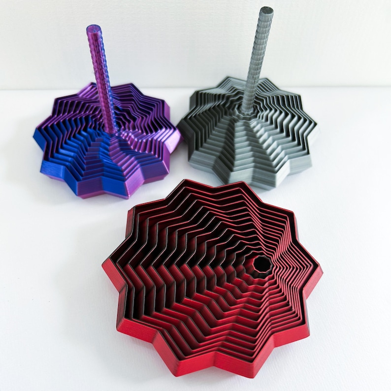 Three 3D printed fidget stars, one in red and black without a handle that is bigger, and two smaller multicolored stars with handles.