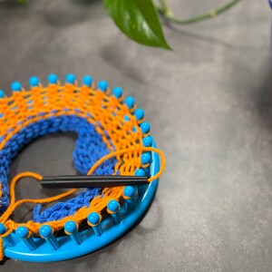black yarn guide feeding orange and blue yarn into round blue knitting loom