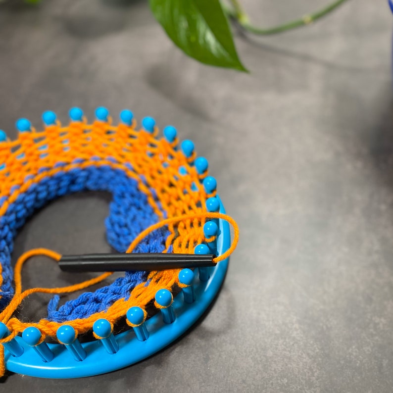 black yarn guide feeding orange and blue yarn into round blue knitting loom