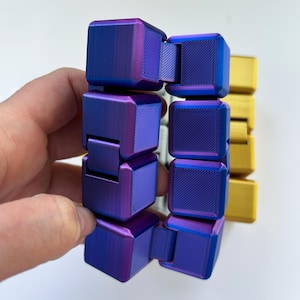 May include: A multi-colored fidget toy with a metallic finish. The toy is composed of connected cubes in shades of purple, blue, and gold. The cubes have a textured surface and are held in place by hinges, allowing for flexible movement.