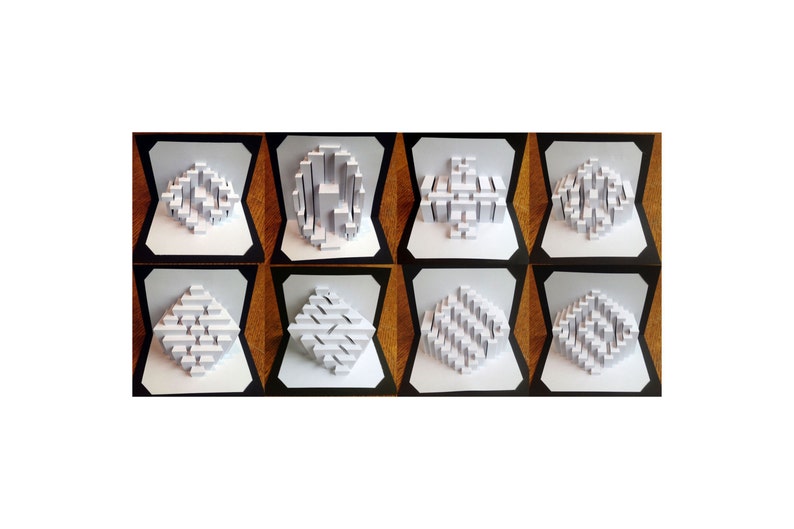 May include: Eight white paper 3D pop-up cards with geometric designs. The cards are displayed in a row on a wooden surface.