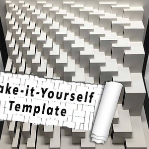 Op de afbeelding: Een wit 3D-model van een geometrisch patroon gemaakt van gestapelde kubussen. Het model bevindt zich in een zwart frame en heeft een gescheurd stuk papier met de tekst "Maak-het-zelf sjabloon" erop.