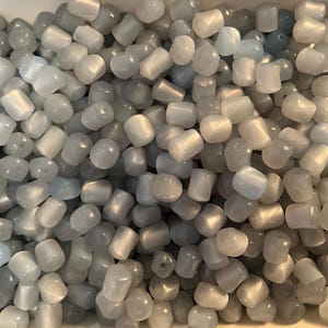 May include: A large quantity of light blue and white cat eye beads. The beads are smooth and have a slightly iridescent finish.