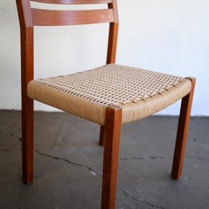 May include: A wooden chair with a woven seat. The chair has a rectangular seat with a woven pattern, supported by four wooden legs. The backrest features two horizontal wooden slats. The chair is made of a warm brown wood.