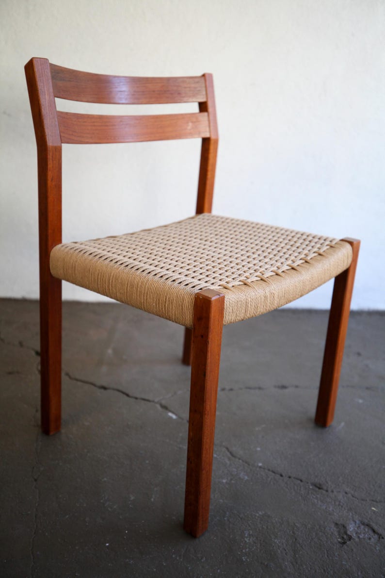 May include: A wooden chair with a woven seat. The chair has a rectangular seat with a woven pattern, supported by four wooden legs. The backrest features two horizontal wooden slats. The chair is made of a warm brown wood.