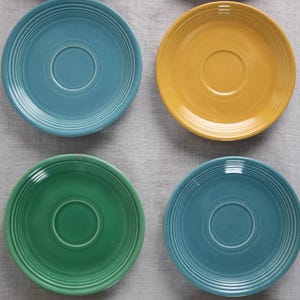 May include: Set of ten colorful ceramic saucers with a raised rim and a center well. The saucers are in shades of blue, green, yellow, and cream.