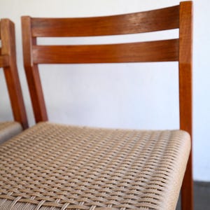 May include: Wooden chair with a woven seat. The chair has a curved back with two horizontal slats. The frame is a warm brown color, and the seat is made of a light tan woven material.