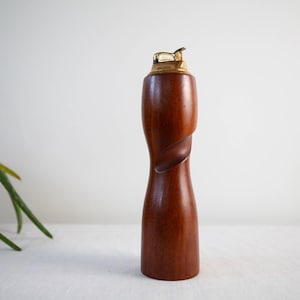 May include: A wooden cigarette lighter with a brass top. The lighter is a dark brown color and has a twisted design.